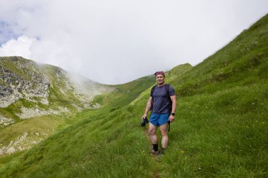 Orta yaşlı bir adam dağda yürüyor.
