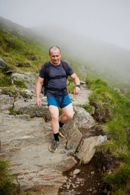 Orta yaşlı bir adam dağda yürüyor.