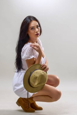 Uzun esmer saçlı, şapkalı, stüdyoda poz veren güzel bir kadının portresi..