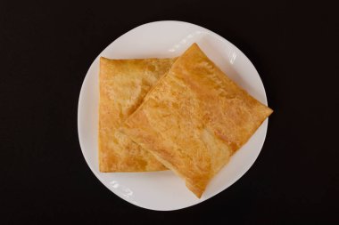 (Siyah arka planda beyaz tabakta peynirli turta..