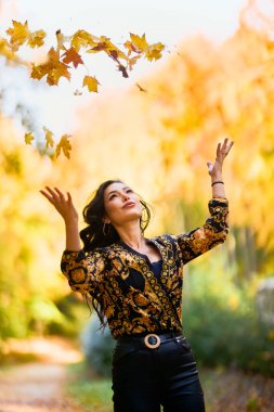 Battaniyeli güzel kadın sonbaharın tadını çıkarıyor ve yaprakların tadını çıkarıyor..
