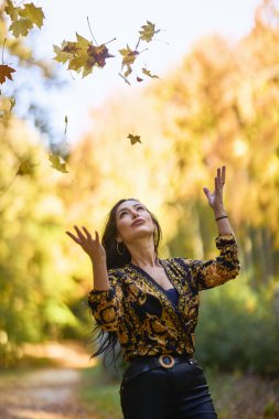 Battaniyeli güzel kadın sonbaharın tadını çıkarıyor ve yaprakların tadını çıkarıyor..