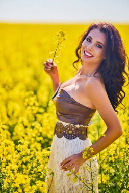 Güzel kadın çiçek açan kolza tohumu tarlasında poz veriyor.