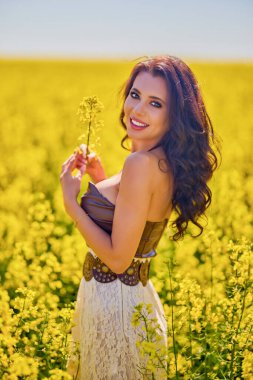 Güzel kadın çiçek açan kolza tohumu tarlasında poz veriyor.