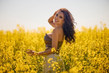 Güzel kadın çiçek açan kolza tohumu tarlasında poz veriyor.