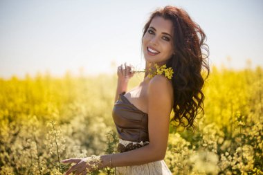 Güzel kadın çiçek açan kolza tohumu tarlasında poz veriyor.
