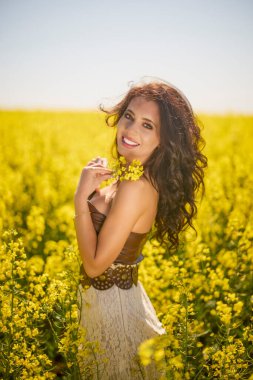 Güzel kadın çiçek açan kolza tohumu tarlasında poz veriyor.