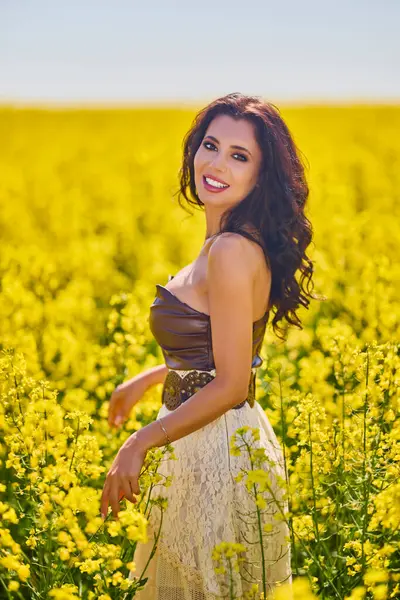 Güzel kadın çiçek açan kolza tohumu tarlasında poz veriyor.