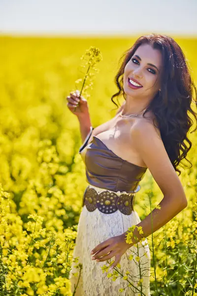Güzel kadın çiçek açan kolza tohumu tarlasında poz veriyor.