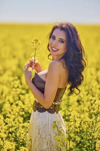 Güzel kadın çiçek açan kolza tohumu tarlasında poz veriyor.