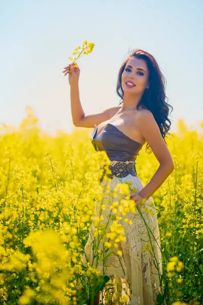Güzel kadın çiçek açan kolza tohumu tarlasında poz veriyor.