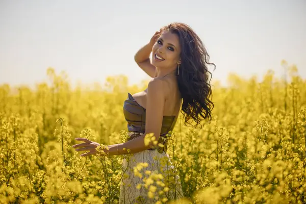 Güzel kadın çiçek açan kolza tohumu tarlasında poz veriyor.