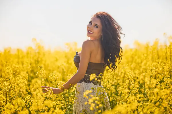 Güzel kadın çiçek açan kolza tohumu tarlasında poz veriyor.