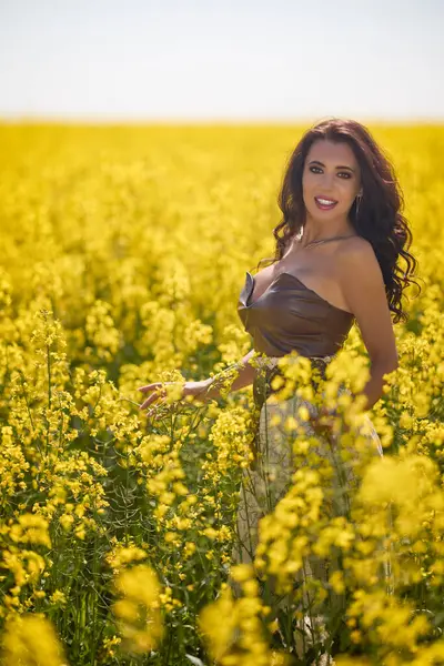 Güzel kadın çiçek açan kolza tohumu tarlasında poz veriyor.