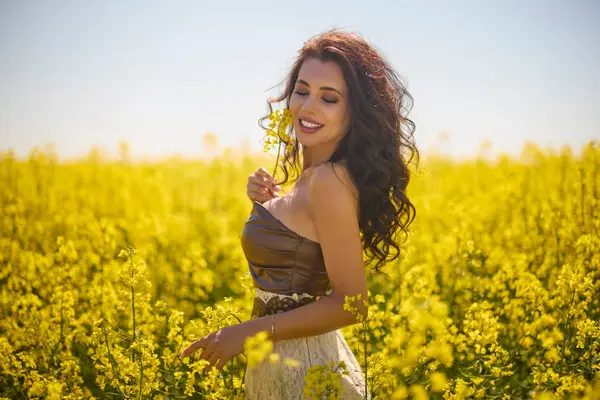 Güzel kadın çiçek açan kolza tohumu tarlasında poz veriyor.