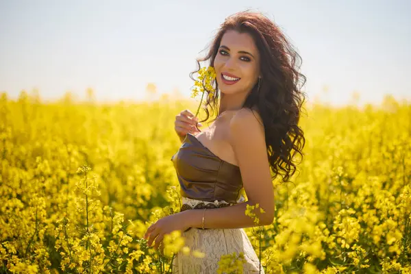 Güzel kadın çiçek açan kolza tohumu tarlasında poz veriyor.