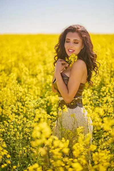 Güzel kadın çiçek açan kolza tohumu tarlasında poz veriyor.