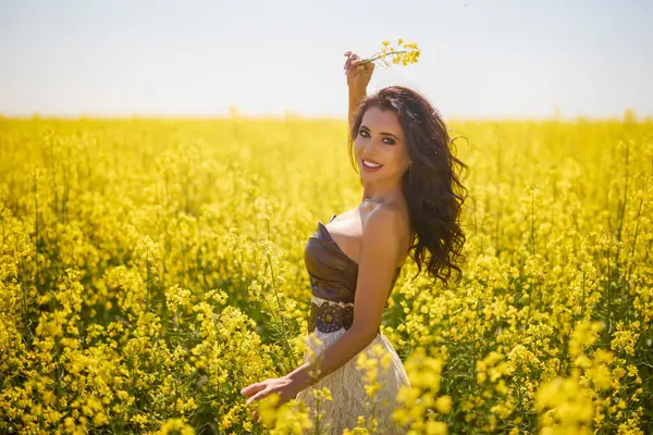 Güzel kadın çiçek açan kolza tohumu tarlasında poz veriyor.