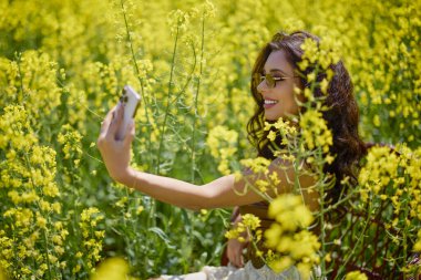 Güzel kadın çiçek açan kolza tohumu tarlasında poz veriyor.