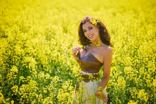 Güzel kadın çiçek açan kolza tohumu tarlasında poz veriyor.