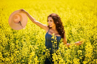 Güneşli bir günde çiçek açan kolza tarlasında poz veren şapkalı güzel bir kadın.