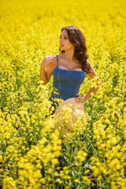 Güneşli bir günde çiçek açan kolza tarlasında poz veren şapkalı güzel bir kadın.