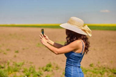 Güneşli bir günde kolza tohumu tarlasında selfie çeken güzel bir kadın.