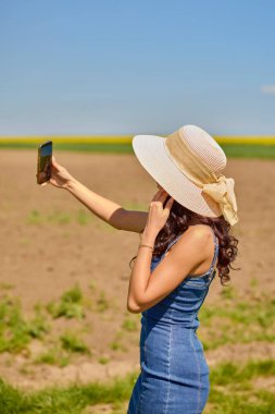 Güneşli bir günde kolza tohumu tarlasında selfie çeken güzel bir kadın.