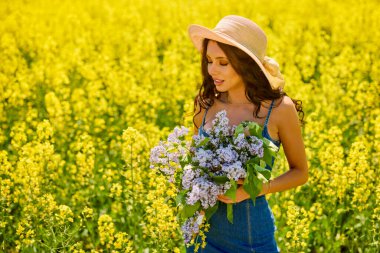 Şapkası ve dalları olan güzel bir kadın (şırınga vulgaris) çiçek açan kolza tohumu tarlasında