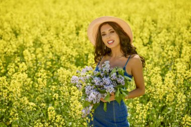 Şapkası ve dalları olan güzel bir kadın (şırınga vulgaris) çiçek açan kolza tohumu tarlasında