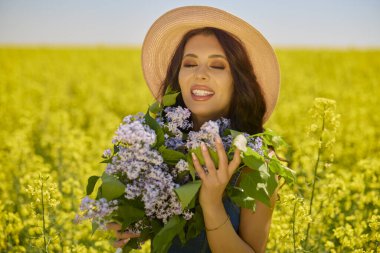 Şapkası ve dalları olan güzel bir kadın (şırınga vulgaris) çiçek açan kolza tohumu tarlasında