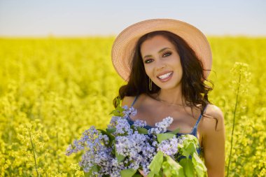 Şapkası ve dalları olan güzel bir kadın (şırınga vulgaris) çiçek açan kolza tohumu tarlasında