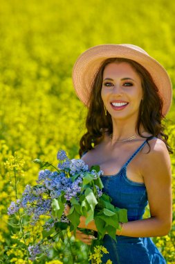 Şapkası ve dalları olan güzel bir kadın (şırınga vulgaris) çiçek açan kolza tohumu tarlasında