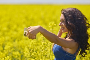 Güneşli bir günde kolza tohumu tarlasında selfie çeken güzel bir kadın.