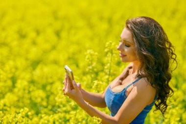 Güneşli bir günde kolza tohumu tarlasında selfie çeken güzel bir kadın.