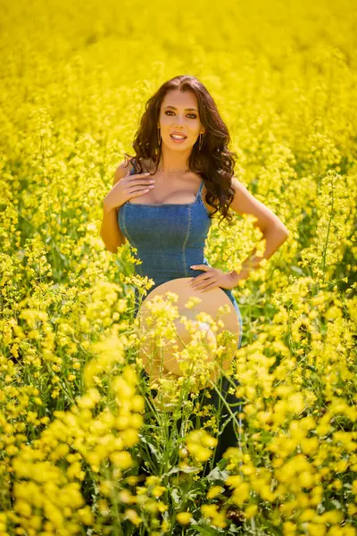 Güneşli bir günde çiçek açan kolza tarlasında poz veren şapkalı güzel bir kadın.