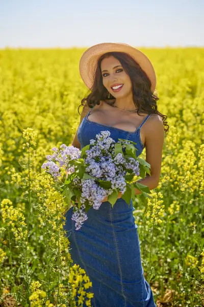 Şapkası ve dalları olan güzel bir kadın (şırınga vulgaris) çiçek açan kolza tohumu tarlasında