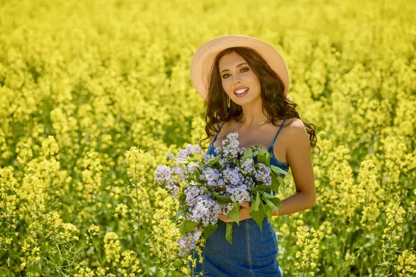 Şapkası ve dalları olan güzel bir kadın (şırınga vulgaris) çiçek açan kolza tohumu tarlasında