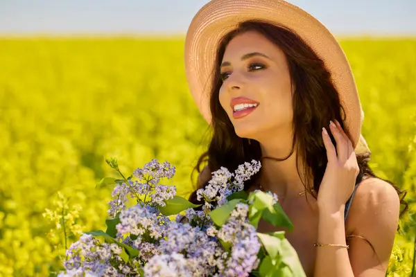 Şapkası ve dalları olan güzel bir kadın (şırınga vulgaris) çiçek açan kolza tohumu tarlasında