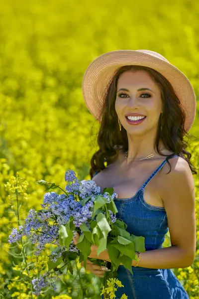 Şapkası ve dalları olan güzel bir kadın (şırınga vulgaris) çiçek açan kolza tohumu tarlasında