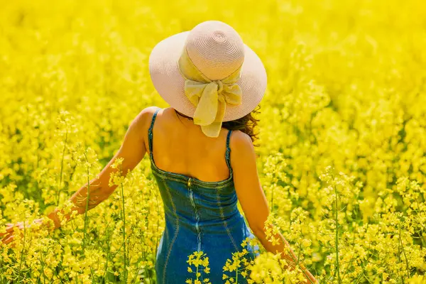Güneşli bir günde çiçek açan kolza tarlasında poz veren şapkalı güzel bir kadın.