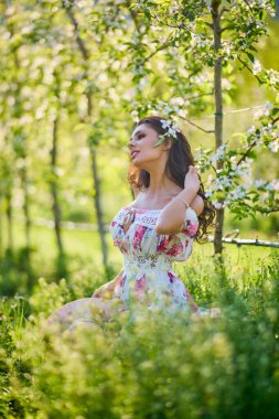 Çiçekli bir elma bahçesinde elbise giymiş güzel bir kadının portresi güneşli bir bahar gününün tadını çıkarıyor.