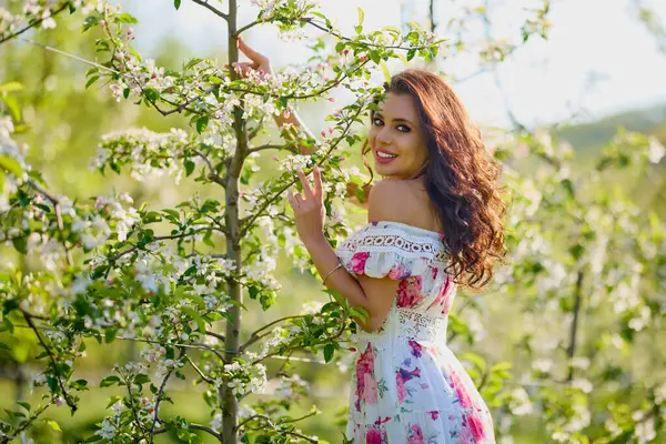 Çiçekli bir elma bahçesinde elbise giymiş güzel bir kadının portresi güneşli bir bahar gününün tadını çıkarıyor.