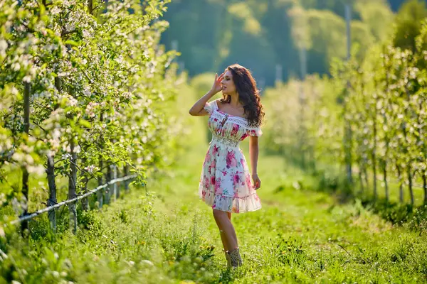 Güneşli bir bahar gününde çiçek açan bir elma bahçesinde güzel bir kadının vücut portresi.