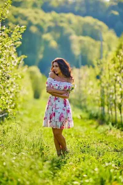 Güneşli bir bahar gününde çiçek açan bir elma bahçesinde güzel bir kadının vücut portresi.