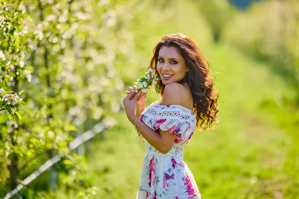 Çiçekli bir elma bahçesinde elbise giymiş güzel bir kadının portresi güneşli bir bahar gününün tadını çıkarıyor.