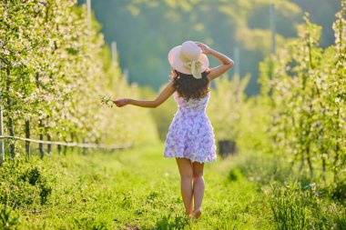 Arkaplanı bulanık, çiçek açmış bir elma bahçesinde güzel bir kadının vücut portresi.