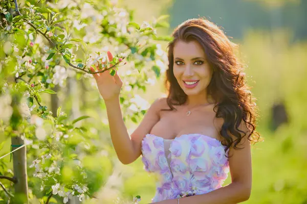 Arkaplanı bulanık, çiçek açmış bir elma bahçesinde güzel bir kadının portresi.