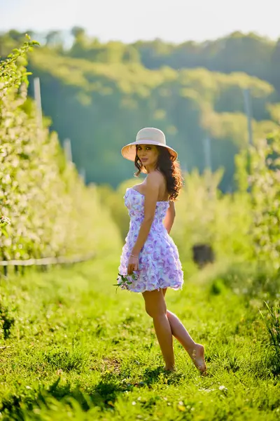 Arkaplanı bulanık, çiçek açmış bir elma bahçesinde güzel bir kadının vücut portresi.