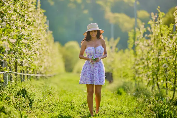 Arkaplanı bulanık, çiçek açmış bir elma bahçesinde güzel bir kadının vücut portresi.